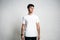 Young handsome guy wearing white blank t-shirt, horizontal studio portrait, empty wall