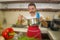 Young handsome and happy man in red apron holding cooking pot smiling cheerful preparing yummy stew smelling delicious aroma in