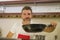 Young handsome and happy man in red apron holding smoking cooking pan smiling cheerful preparing yummy stew smelling delicious