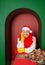 Young handsome happy man wearing Santa hat and yellow mittens on Christmas gift box in the green arch background