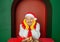 Young handsome happy man wearing Santa hat and yellow mittens on Christmas gift box in the green arch background