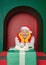 Young handsome happy man wearing Santa hat and yellow mittens looking on Christmas gift box in the green arch background