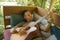 Young handsome and happy mixed ethnicity man in hipster style chilling outdoors playing guitar relaxed at tranquil tropical garden