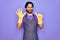 Young handsome hispanic clenaer man wearing housework apron and washing gloves showing and pointing up with fingers number six