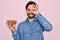 Young handsome hispanic man with bear holding natural ingredient healthy almonds with happy face smiling doing ok sign with hand