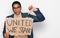 Young handsome hispanic man holding united we stand banner with angry face, negative sign showing dislike with thumbs down,