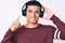 Young handsome hispanic man listening to music using headphones smiling happy pointing with hand and finger to the side