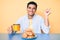 Young handsome hispanic man sitting on the table having breakfast smiling happy pointing with hand and finger to the side