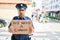 Young handsome hispanic policeman wearing police uniform with serious expression holding we need a change banner at town street