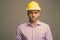 Young handsome Indian businessman wearing hardhat against gray background