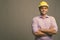 Young handsome Indian businessman wearing hardhat against gray background