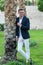 Young handsome laughing man in a white shirt, white trousers and suit stands near the palm tree