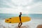 Young handsome male surfer with a surfboard is enjoying a view while walking a sandy beach at sea. Summer, vacation, ocean.