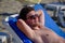 A young handsome man of 25-30 years old, a brunette, in weed sunglasses, lies relaxed on a lounger on a sandy sea beach, takes a