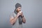 Young handsome man with the beard in grey hat and scarf standing by the grey wall holding cup of coffe or tea in front