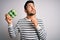 Young handsome man with beard holding carton box of fresh eggs over white background serious face thinking about question, very