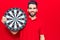 Young handsome man with beard holding dartboard looking positive and happy standing and smiling with a confident smile showing