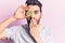 Young handsome man with beard holding kiwi over eye covering mouth with hand, shocked and afraid for mistake