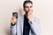 Young handsome man with beard holding police badge covering mouth with hand, shocked and afraid for mistake