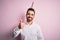 Young handsome man with beard wearing funny unicorn diadem over pink background doing happy thumbs up gesture with hand