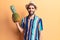 Young handsome man with beard wearing summer hat and shirt holding pineapple looking positive and happy standing and smiling with