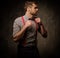 Young handsome man with beard wearing suspenders and bow tie, posing on dark background.