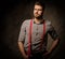 Young handsome man with beard wearing suspenders and posing on dark background.