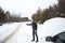 Young handsome man in black jacket in winter, stood on the highway and hitchhiking.