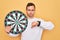 Young handsome man with blue eyes holding dartboard over isolated yellow background with angry face, negative sign showing dislike