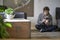 Young handsome man with a cold sitting on the floor in his apartment with a thermometer in his mouth and a cup of tea in his hands