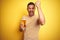 Young handsome man drinking a pint glass of beer over  yellow background annoyed and frustrated shouting with anger, crazy