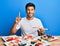 Young handsome man eating sushi sitting on the table smiling with an idea or question pointing finger with happy face, number one