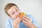 Young handsome man eats fresh tasty burger from fast food restaurant looks hungry on isolated white background