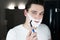 Young handsome man with foam on his face shaving with razor in bathroom in the morning looking serious everyday routine