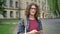 Young handsome man in glasses with long curly hair chatting on phone and standing in park near university building