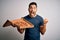 Young handsome man holding delivery box with delicious Italian pizza over white background screaming proud and celebrating victory