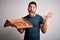 Young handsome man holding delivery box with delicious Italian pizza over white background very happy and excited, winner