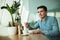 Young handsome man holding fork in his hand eats salad and drinks coffee for lunch during break at cafe near office