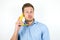 Young handsome man holding one fresh banana as a phone near his ear looks suspicious on isolated white background