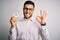 Young handsome man holding reminder paper with pay taxes message over white background doing ok sign with fingers, excellent