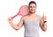 Young handsome man holding tennis racket surprised with an idea or question pointing finger with happy face, number one