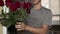 Young handsome man with a little stubble in a gray T-shirt straightens fixing and sniffs a beautiful bouquet of red