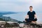 Young handsome man in a meditative position sits on a lawn on a background of forest and sunset. Concept of freedom relaxation.