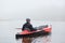 Young handsome man paddling canoe on cloudy day, canoeing on foggy day, back view of extreme sportsman enjoying water sport in