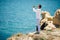 Young handsome Man praying in beautiful inspiring ocean coast enjoy inspirational landscape on rocky top