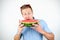 Young handsome man with red eyeglasses on his head biting ripe fresh watermelon on isolated white background