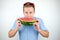 Young handsome man with red eyeglasses on his head biting ripe watermelon on isolated white background