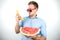 Young handsome man in red eyeglasses with watermelon holding fresh banana like a phone on isolated white background