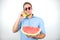 Young handsome man in red eyeglasses with watermelon holding fresh banana like a phone looking happy on isolated white