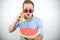 Young handsome man in red eyeglasses with watermelon holding fresh banana like a phone looking surprised on isolated